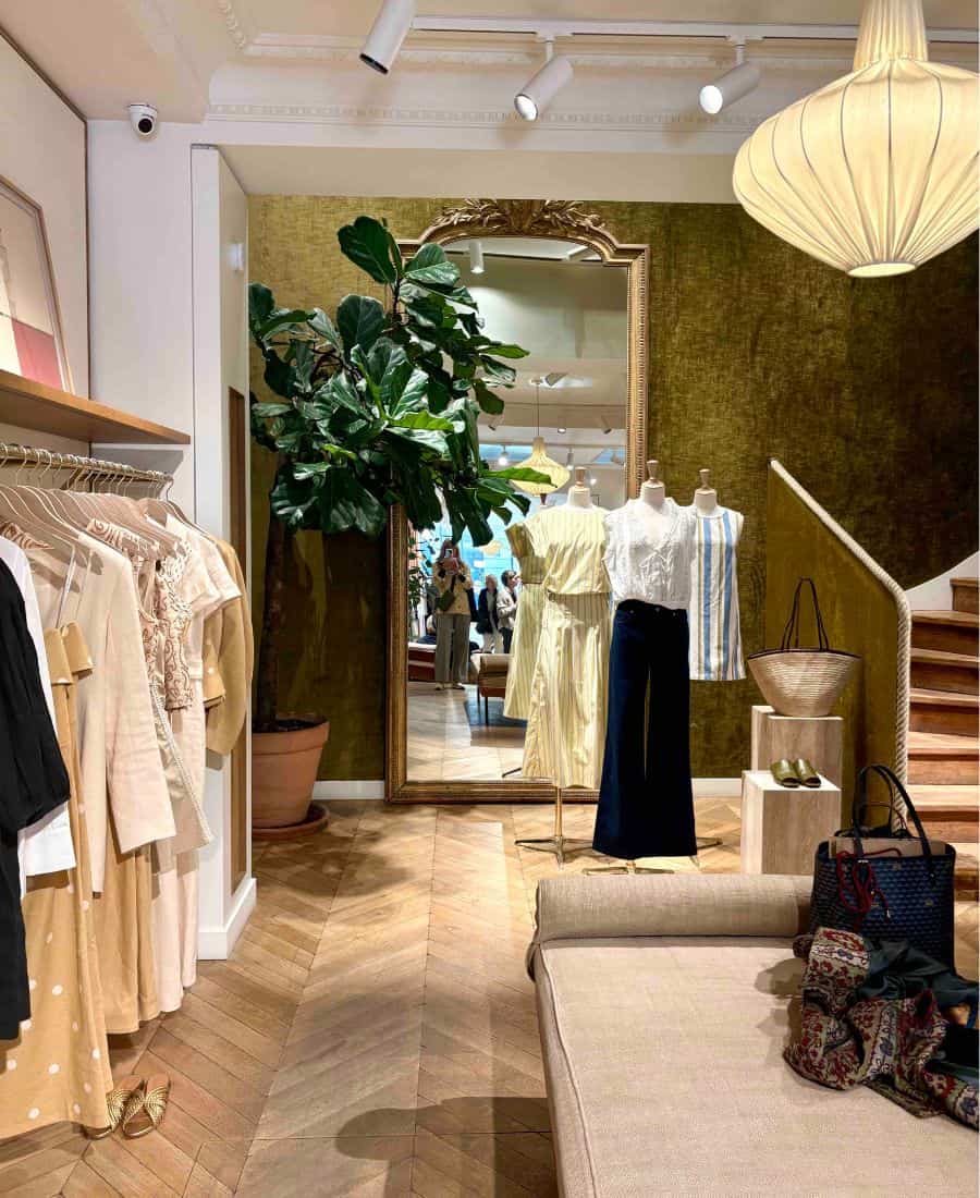 The inside of the Sézane store features a large gold mirror, an elegant hanging light fixture, herringbone wood floors and racks of clothes.