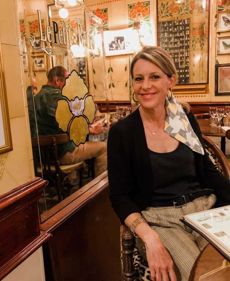 A blonde woman with a scarf tied in her hair sits in a classid French bistro