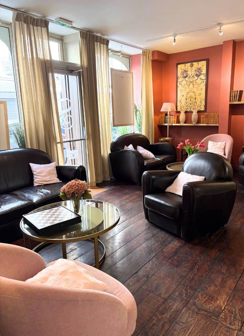 A cheerful hotel lobby with wood floors, armchairs and colorful accents. One wall features large bright windows.