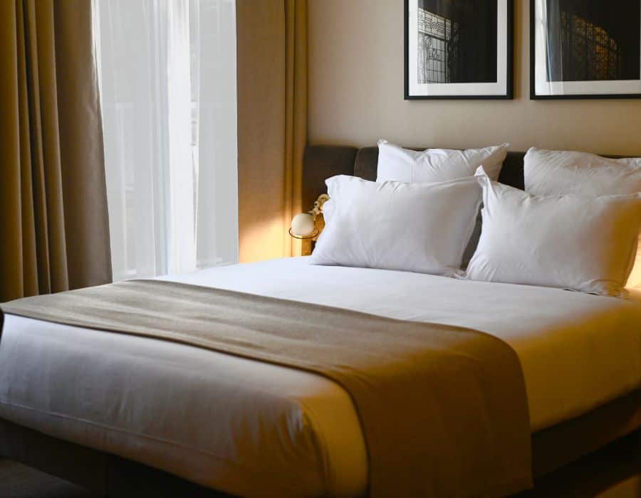 A chic hotel room in beige and brown with a double bed and window partially visible.