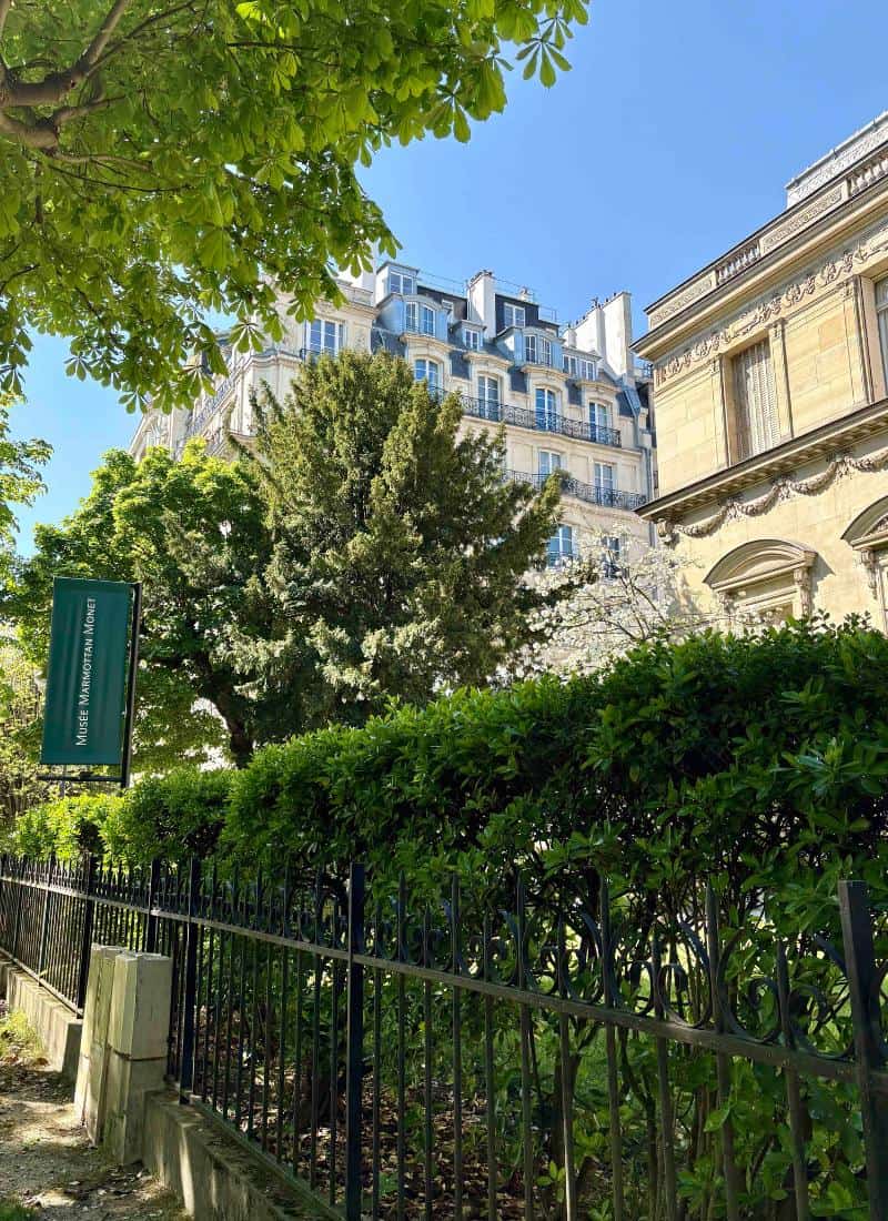 A leafy street in Paris with the Museum Marmottan Monet partly visible among the Paris rooftops.