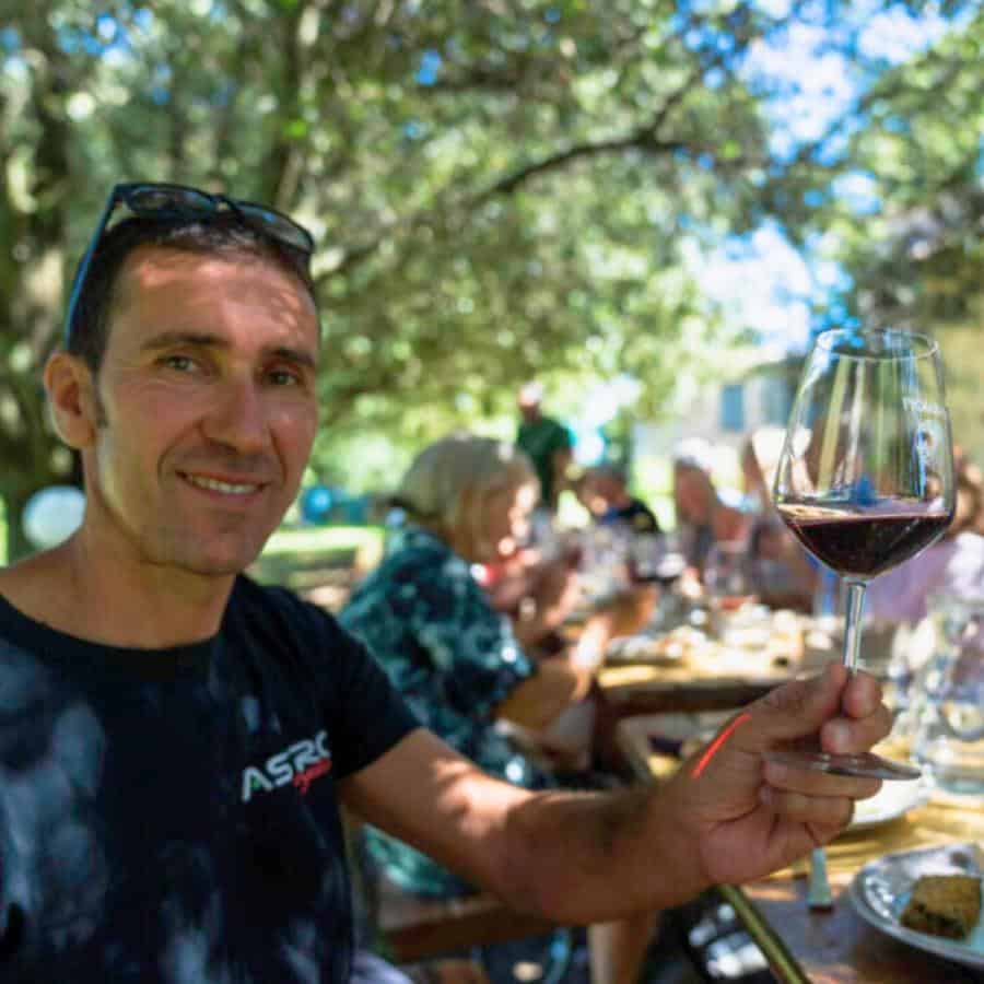 Fabrizio Giacomelli holds a glass of wine with a group of guests at lunch on a guided cycling trip in Italy.