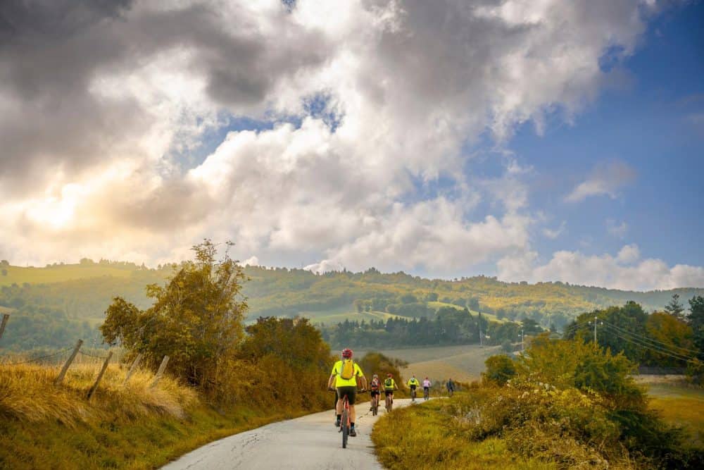 Cyclists follow a winding paved road through a hilly landscape