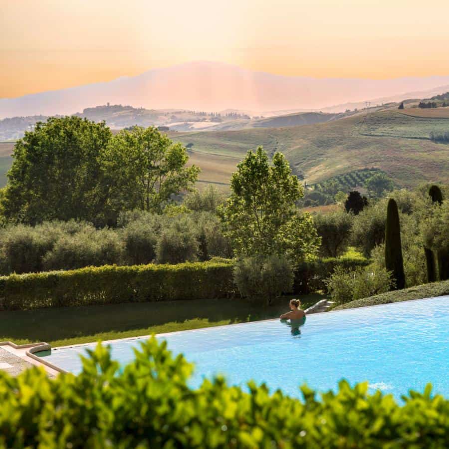 A woman looks out from a pool to the rolling Italian Hills.