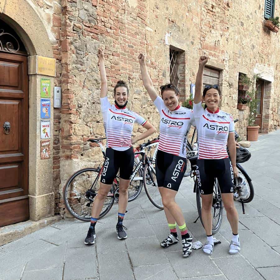 A group of women cyclists stand next to their bikes in a charming town in Italy